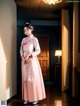 A woman in a pink kimono standing in a hallway.