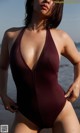 A woman in a maroon one piece swimsuit standing on the beach.