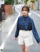 A woman in a blue shirt and white shorts walking down a street.