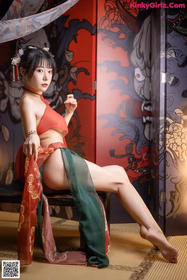 A woman in a red and green kimono sitting on a chair.