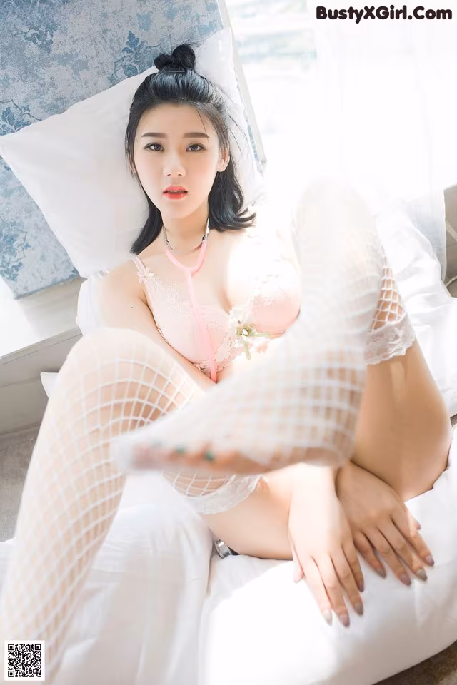 A woman in a pink lingerie sitting on a bed.