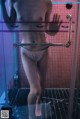 A woman in a white thong standing in a shower.