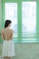 A woman in a white dress standing in front of a window.