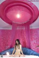 A naked woman sitting on a bed in a pink room.