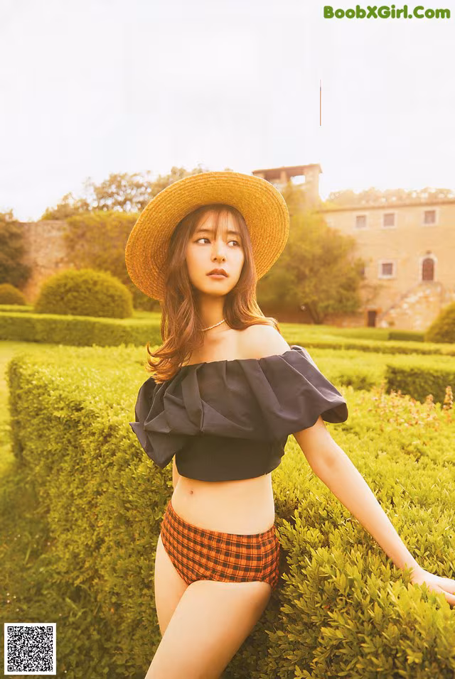 A woman in a straw hat sitting on a hedge.