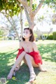 A woman in a red dress sitting under a tree.