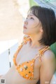 A woman in an orange bikini sitting on a bench.